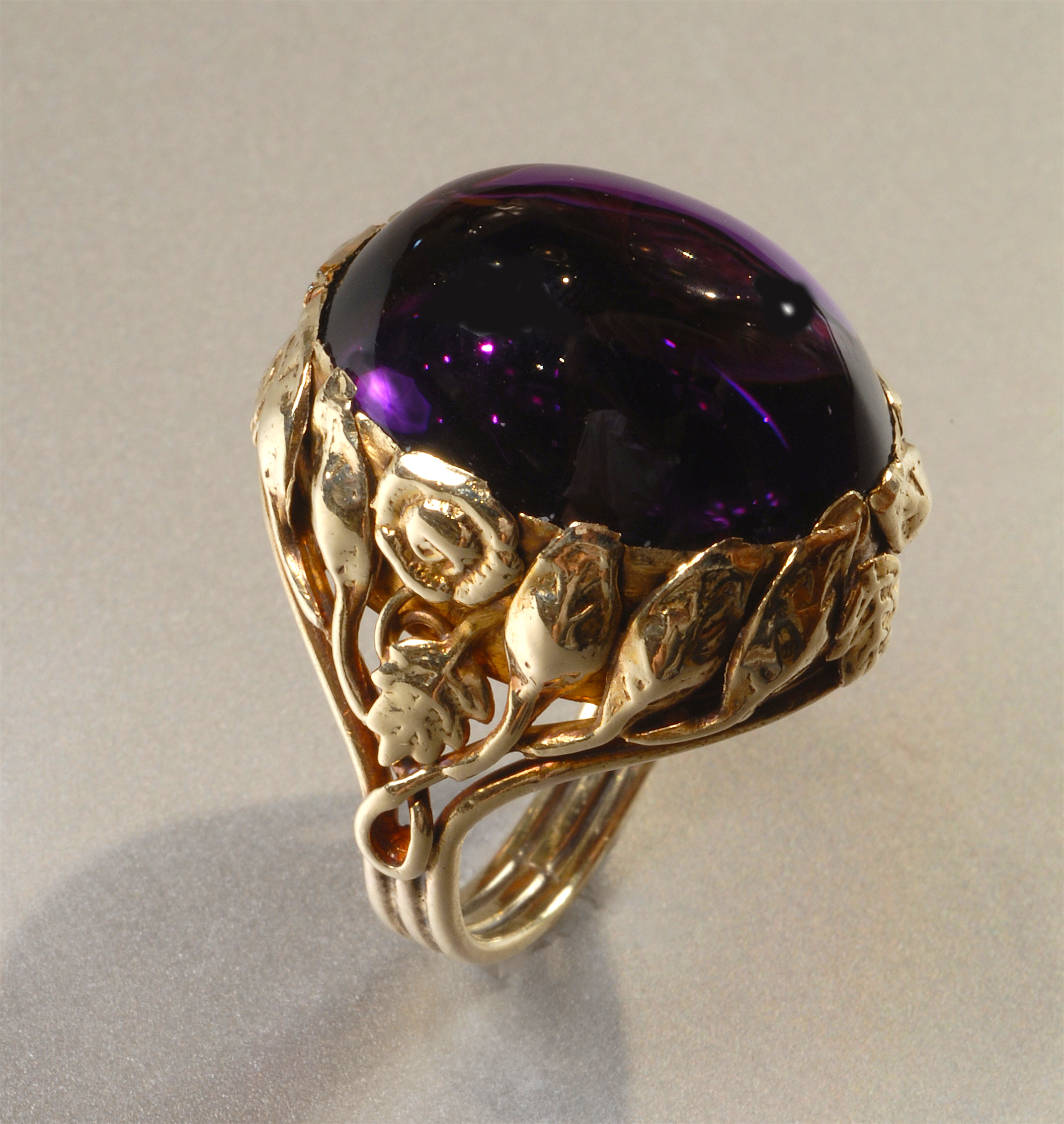 American Arts & Crafts ring, detailed and scrolling 14K gold mount with stylized leaves and blossoms surrounding a large cabochon amethyst (approx. 22+ carats TW), marked, c. 1915