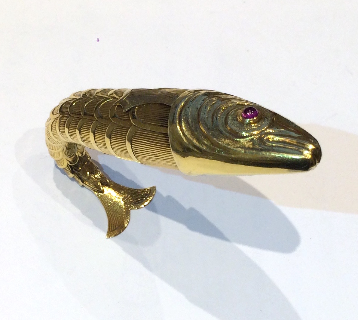 Jean Schlumberger, Paris, famous articulated “fish” lighter, 18K gold body and tail composed of striated and scallop edged scales, set with two cabochon sapphires for eyes, one pink and one blue, signed: Schlumberger, Modele Depose, French Eagle’s head touch mark for 18k gold (3x), Crab mark for silver made in the French provinces, (lighter insert only) c. 1939-42   Model illustrated: The Jewels of Jean Schlumberger, catalogue no. 50