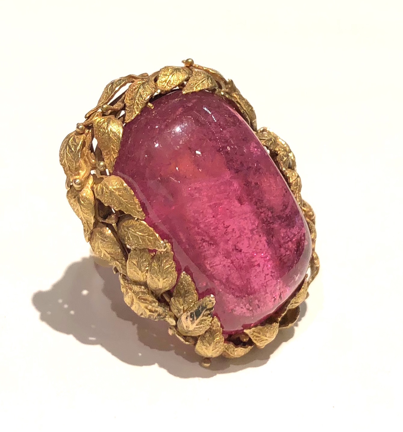 American Arts & Crafts ring (most likely Boston School) set with a large rectangular shaped pink tourmaline cabochon (approx. 54 carats) set in an elaborate 18k gold handwrought mounting with a garland surround of leaves and scrolling structural ring shank support, c. 1915
