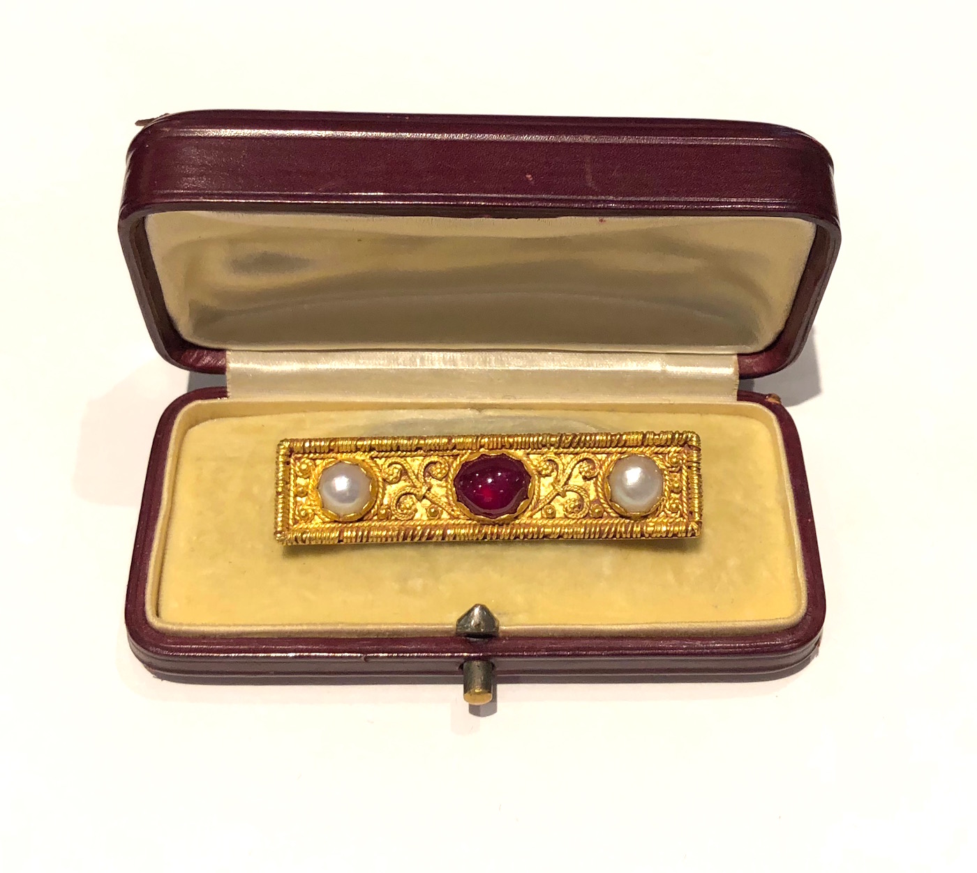 Jules & Louis Wiese Etruscan Revival brooch set with a gem quality cabochon ruby (approx. 4.32 carats by calculation) and two natural pearls (7mm each) all in an elaborate 18k gold mount with intricate twisted scrolls and a gold wire wrapped border signed: Wiese (in Gothic-style signature mark), French diamond maker’s poincon, French Eagle’s head mark for 18k gold, original burgundy leather presentation box with fancy embossed gilt initials on the cover and a vanilla silk velvet and satin interior, c.1875