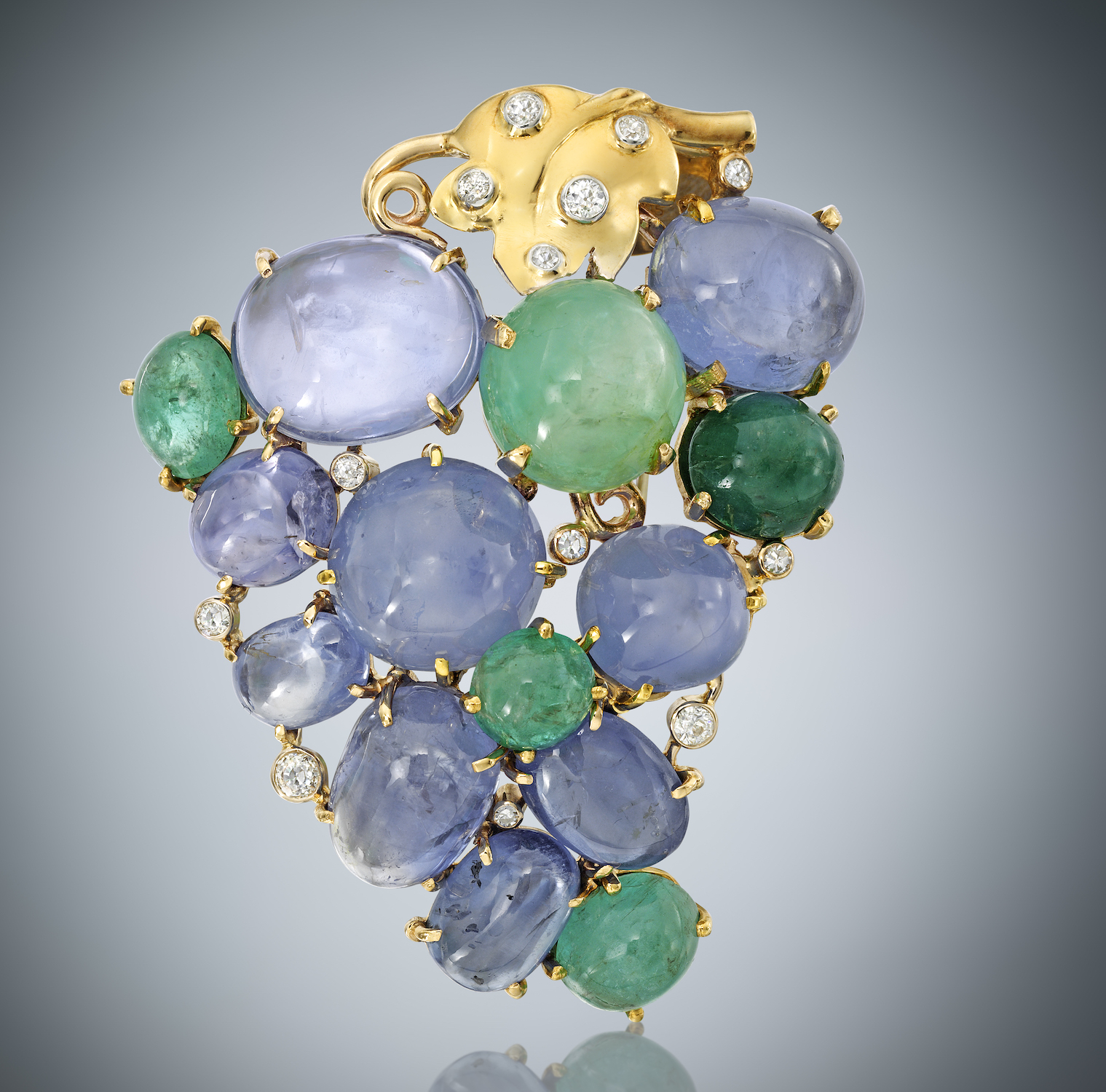 Seaman Schepps “Grape” cluster clip/brooch set with 9 large cabochon sapphires (approx. 85+ carats TW), 5 large cabochon emeralds (approx. 35+ carats TW) and 13 round diamonds (approx. 2 carats TW) set in a 14K yellow mounting with leaves and vines, signed Seaman Schepps and 14k, Dimensions: 2 3/4 inches long x 2 1/4 inches wide, c. 1940