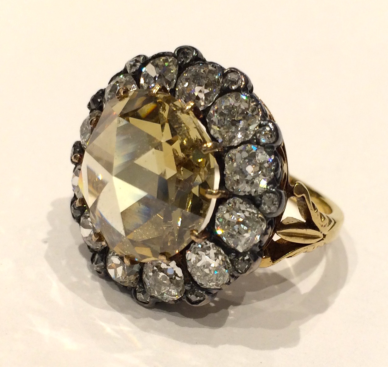 Champagne “Mughal” Diamond ring, Round rose cut fancy light to fancy brownish yellow natural color center diamond (G.I.A. certificate, 5.50 carats) encircled with 12 old mine cut brilliant diamonds (G.I.A. certificate, near colorless approx. 8 carats TW) and 12 small round old mine cut diamonds all set in white and yellow gold, mid 19th Century