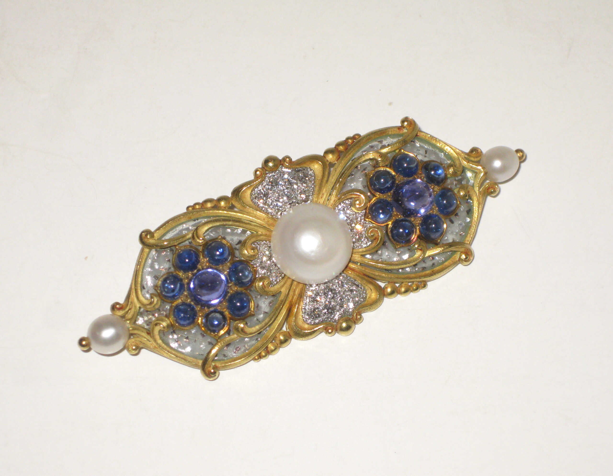 Marcus & Co. Art Nouveau brooch, “Tibula” shaped 18k yellow gold brooch set with three natural pearls, the natural center button pearl approx. 10 mm in diameter (G.I.A. certificate, 3 natural freshwater pearls, weight 24.90 grams, measurement range from 5.46 to 12.26mm), 16 sugarloaf cabochon sapphires, the two large and high dome middle sapphires with a purple hue, 20 pave set round diamonds all surrounded with clear plique-a-jour further trapped with platinum flakes, signed c. 1897